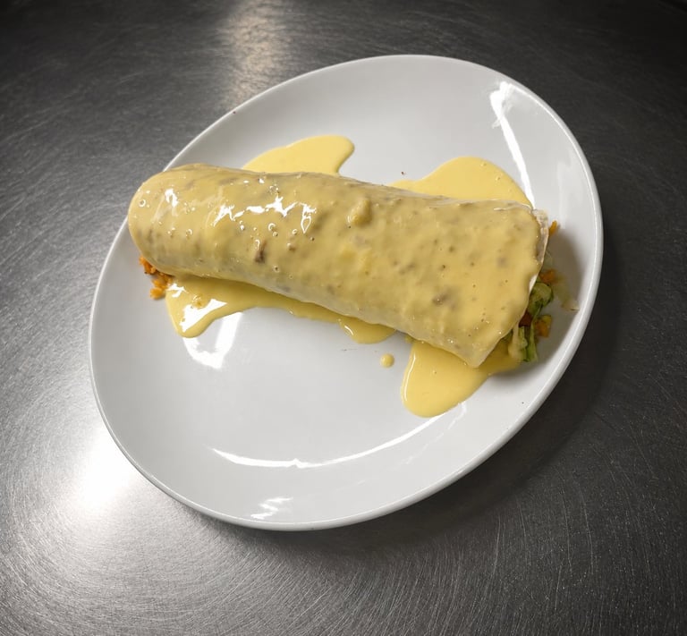 A rolled crepe or omelet filled with ingredients, served on a white plate with yellow sauce drizzled on top